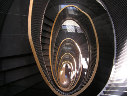 Palais Leopold - Blick von oben auf eine oval scheinende dunkle Treppe mt goldenem Handlauf