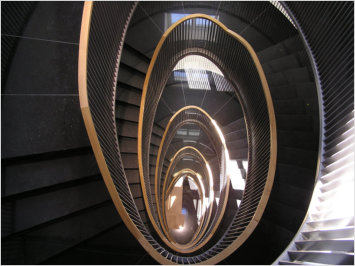 Palais Leopold - Blick von oben auf eine oval scheinende dunkle Treppe mt goldenem Handlauf